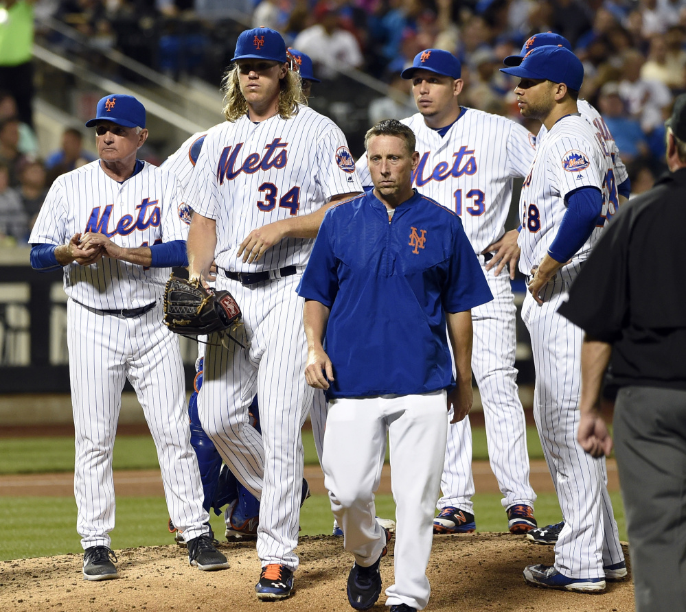 Mets Manager Terry Collins, left, looks to the dugout as a trainer escorts injured starting pitcher Noah Syndergaard from the mound Friday night.