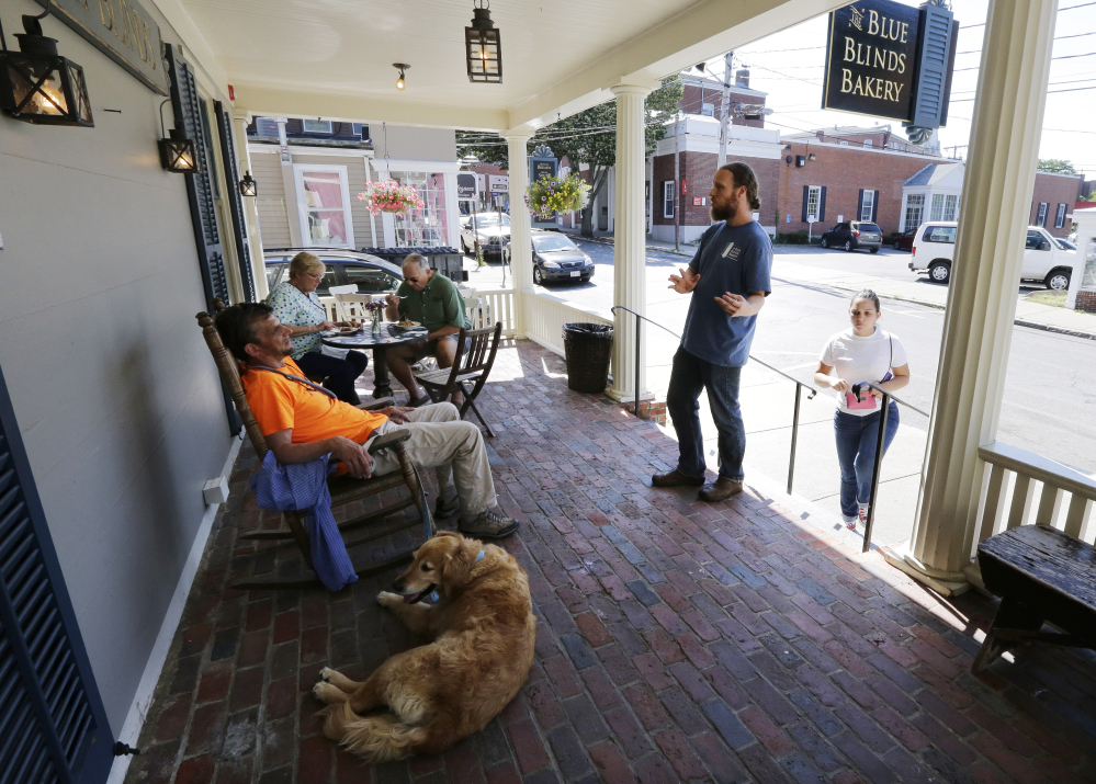 Lev Bryant, manager of the Blue Blinds Bakery, right, engages a customer in a cordial conversation regarding faith on the front porch of the bakery, Wednesday, in Plymouth, Mass. The bakery is owned by a Christian sect, The Twelve Tribes.