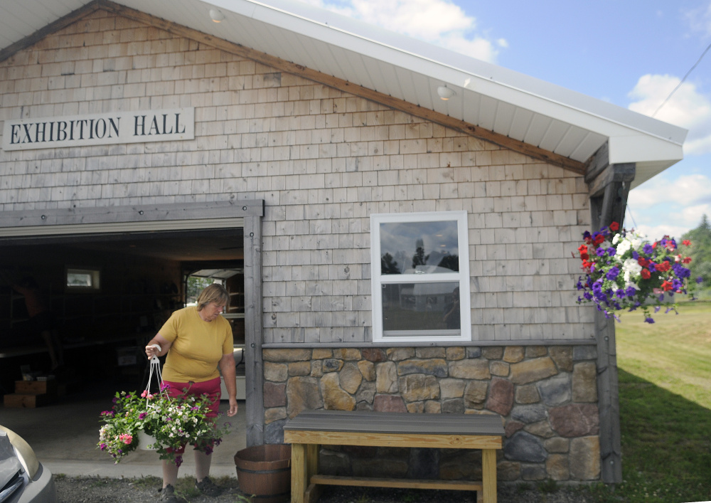 Jean Ambrose hangs flower baskets Tuesday on the exterior of the Exhibition Hall at the Pittston Fair, which runs Thursday through Sunday.