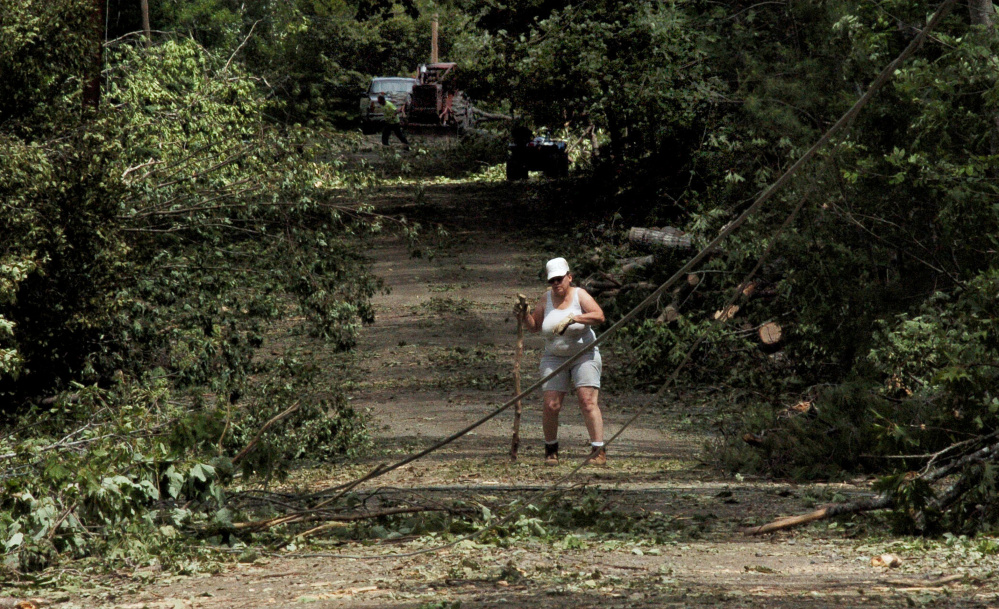 Ballard Road resident Luanne Paquin works to clear brush around utility wires and broken poles on the closed road in St. Albans on Tuesday. The road was filled with fallen trees, wires and utility poles following a severe storm Monday. A skidder machine and operator in background clear trees from the roadway.