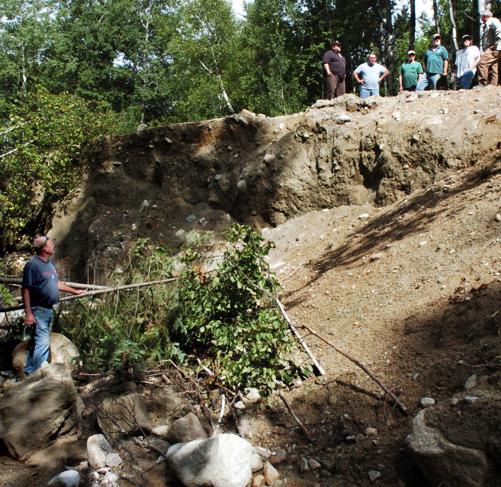 Russ Flagg, left, a landowner and board member of Mile 10 Owners Road Association looks up to a delegation of other landowners and officials on top of the washed-out Old Spencer Road in Upper Enchanted Township. The group surveyed the storm damage made last month in the area and looked at ways to fix roads that were washed out in a June storm.