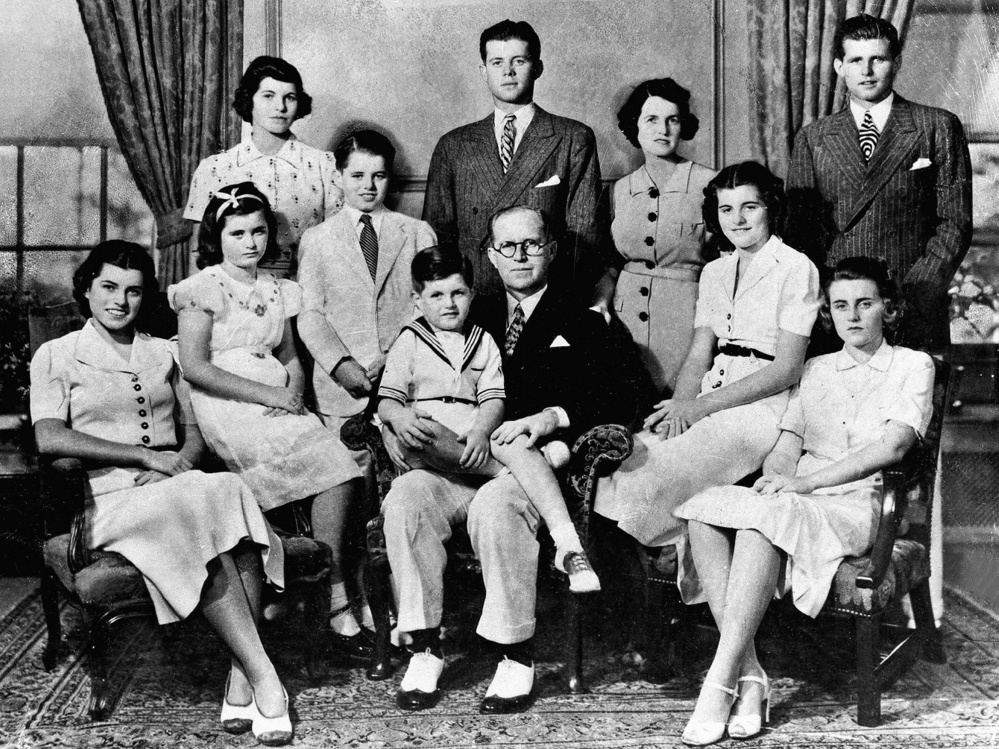 Joe and Rose Kennedy with their nine children. Bobby is wearing a light-colored suit and standing behind Ted, who is sitting on his father's lap.