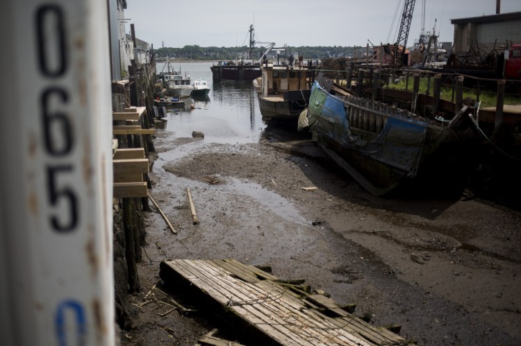 Boats lie in silt during low tide at Sturdivant's Wharf along Portland Harbor. Numerous public and private wharves have lost valuable berthing spaces as silt carried down the Fore River and from occasional sewer and stormwater runoff has built up around them. 
