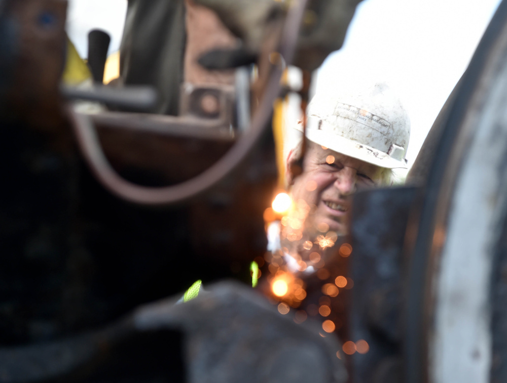A volunteer from New England Steam Corporation watches as a worker cuts the ash plate from the body of the Old 470 locomotive at the rail yard on College Avenue in Waterville on Monday. The train, which has sat for more than 60 years since its last run, will be shipped to Ellsworth by truck to be restored.