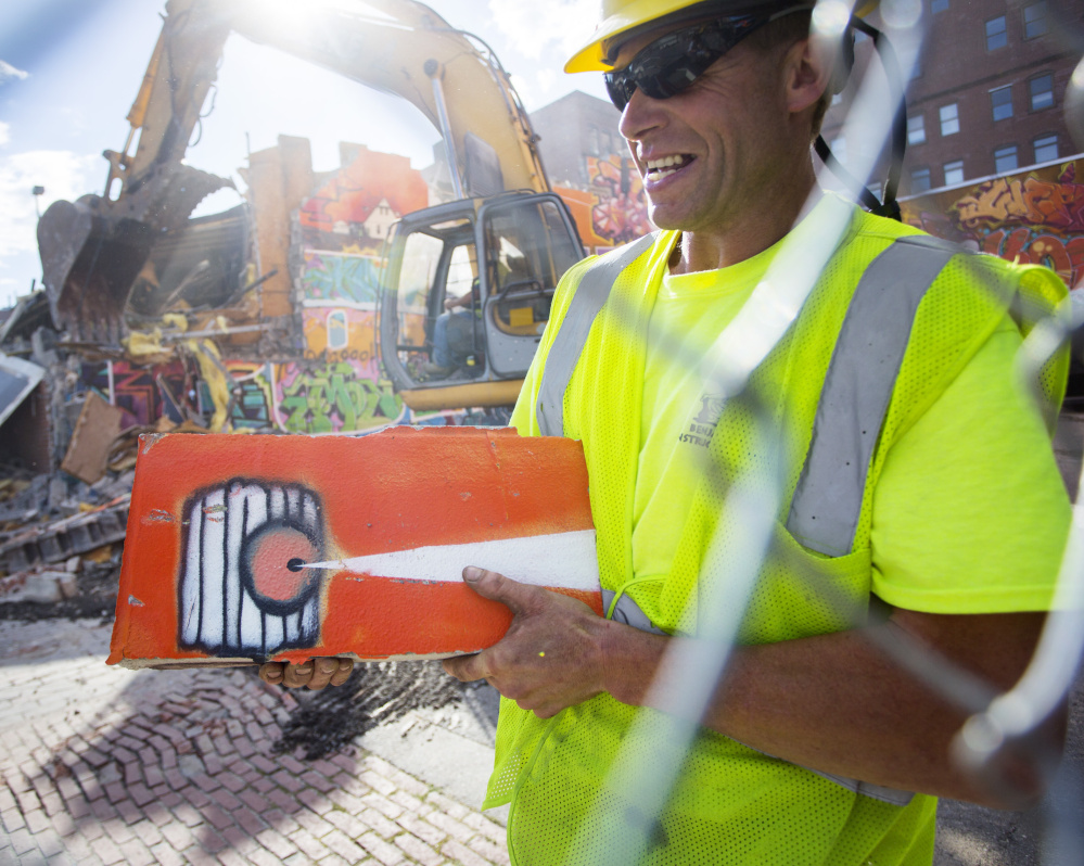 Workers demolish a graffiti wall on Free Street in Portland on Monday. Harry Fillmore of Benjamin Construction holds a piece of the mural.