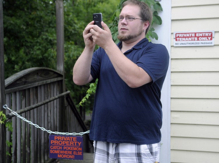 Stephen Turcotte plays Pokémon Go on Monday between signs on a stairwell in Hallowell that indicate the property is private.