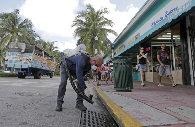 Miami-Dade mosquito control inspector Yasser "Jazz" Compagines sprays a chemical mist into a storm drain Tuesday as a tour vessel passes by in Miami Beach. Bermuda, among other places, is seeing an uptick in visitors.