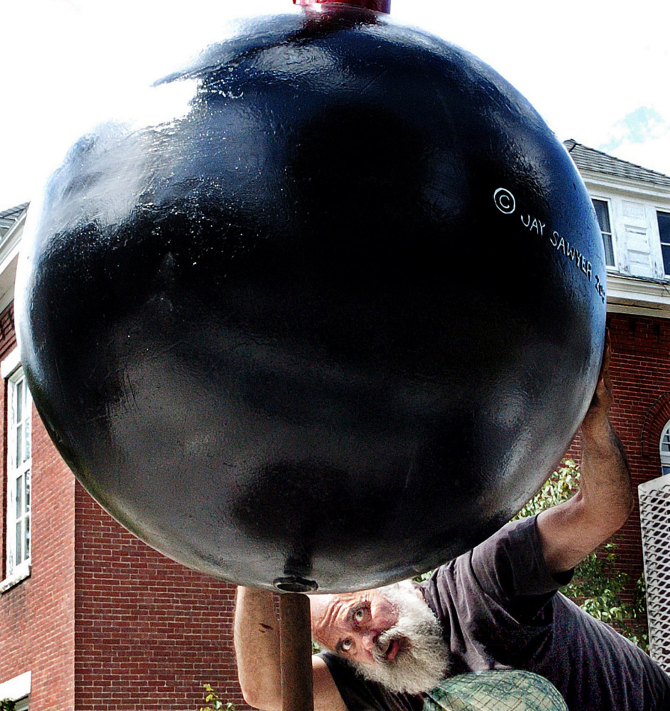 Sculptor Jay Sawyer, shown Thursday, gets under his sculpture "F Bomb," part of his exhibit at the Emery Community Art Center at the University of Maine in Farmington on. Saywer's exhibit, "Sculpture Soup," uses letters of the alphabet to create wordplay.