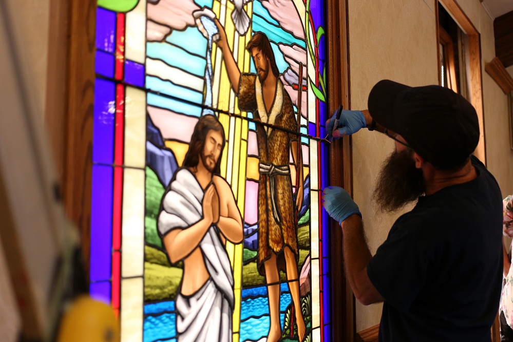 Ruben Llano works on the installation of a handmade glass window Thursday at the Addison Congregational Church in Addison Mich.