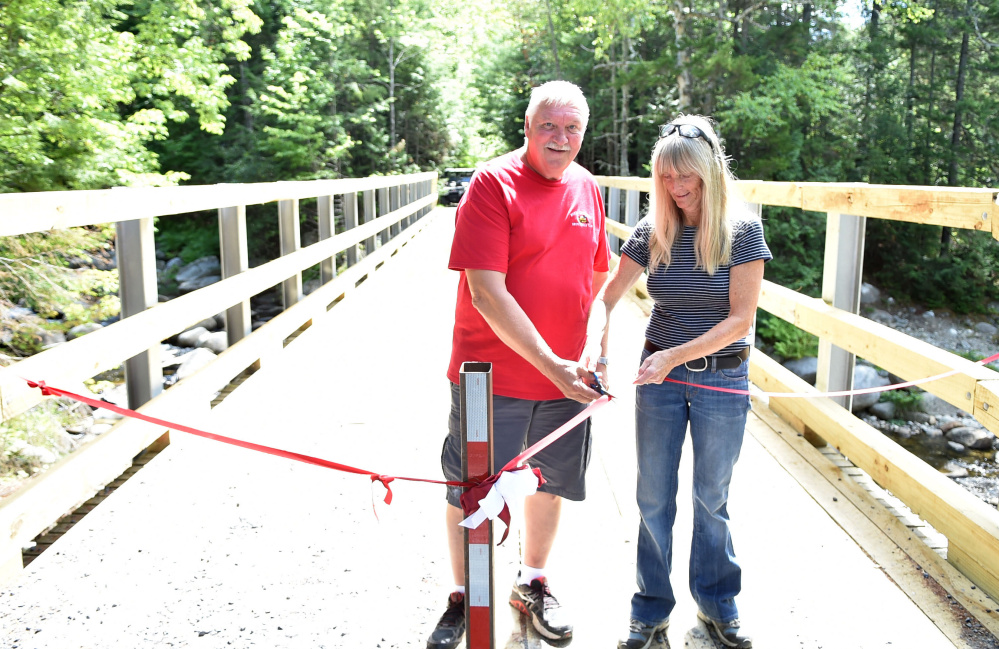 Ralph Luce, president of the North Franklin Snowmobile Club, cuts a ribbon with volunteer Nancy Perlson on Saturday during a ceremony marking the opening of the Perham Stream Bridge in Madrid Township.