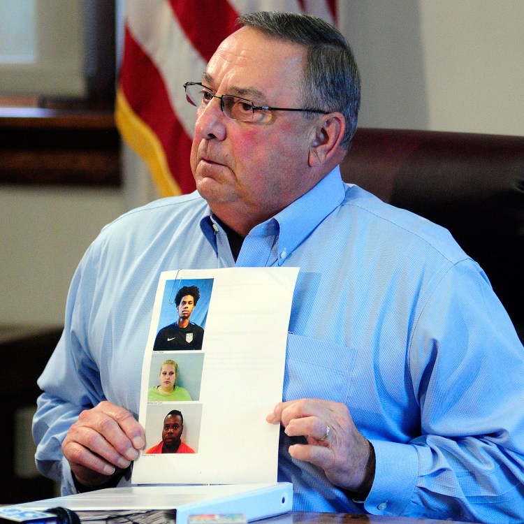 Gov. Paul LePage holds up booking mug shots from a three-ring binder of news releases and articles about drug arrests during a meeting with reporters on Friday in the State House Cabinet room in Augusta.