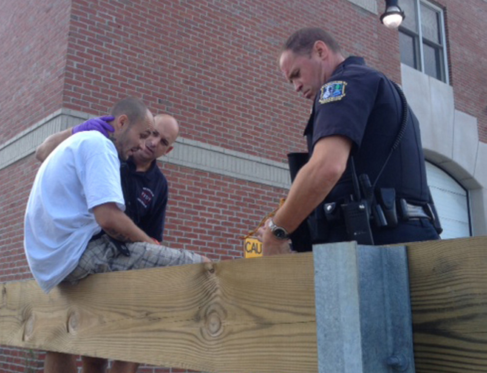 A Waterville firefighter treats a man who was attacked Thursday morning in an apartment on Union Street, with police Officer Matt Libby at right. Police still were looking for the attacker, who reportedly was armed with a gun and a hammer.