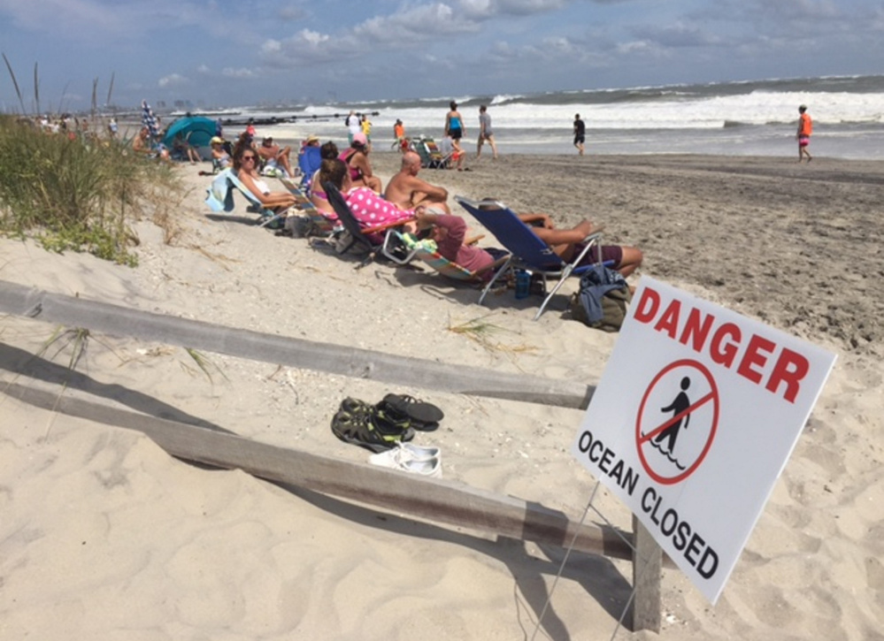 People sit at the beach in Ocean City, N.J., on Sunday as waves roar ashore. Hermine is expected to stay hundreds of miles off the East Coast, delivering large waves and storm surge.