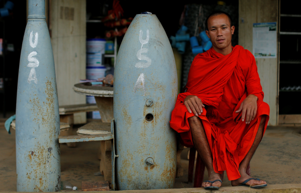 A Buddhist monk sits beside two of the 80,000 unexploded bombs that the U.S. dropped on Laos during the Vietnam War.