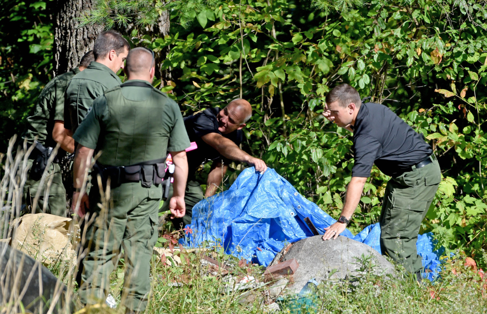 Investigators with the Maine State Police and Maine Warden Service look for evidence in the death of a woman whose body was found in the woods behind 628 Norridgewock Road in Fairfield on Tuesday.