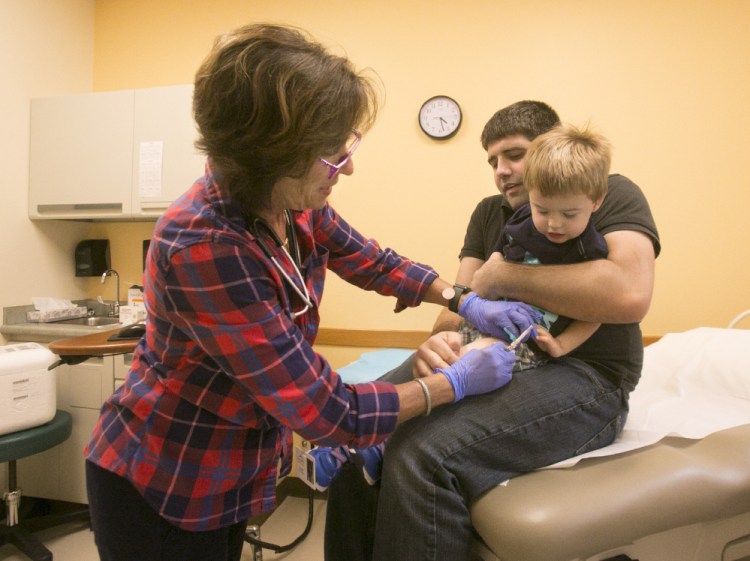 Nurse Kathy Aranson prepares to give a flu shot to Isaac Ambrose, 2, while his father, Chris Ambrose, holds on Friday.