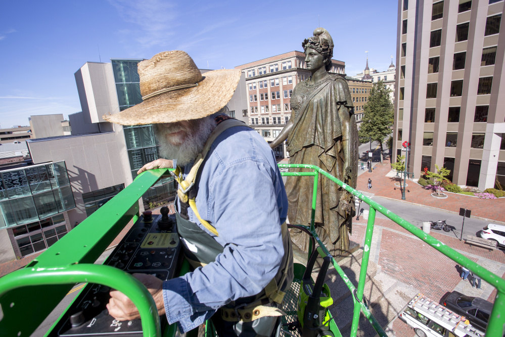 Jonathan Taggart lowers himself to the ground after cleaning part of the "Our Lady of Victories" statue in Monument Square on Monday.