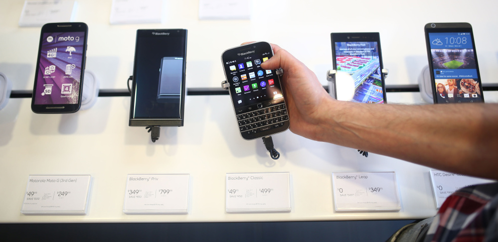 An employee holds a BlackBerry Classic smartphone at a store in Waterloo, Ontario. BlackBerry is handing over production of the phones to overseas partners.