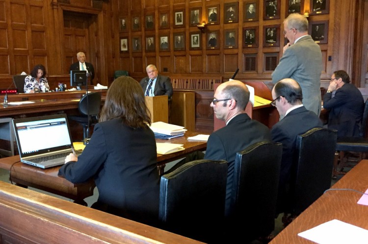 Flanked by his attorneys, Gregory Nisbet, second from left, who is charged with six counts of manslaughter in connection with a 2014 fire at a Portland apartment building that he owned, listens to Assistant Attorney General John Alsop question Daniel Young, an investigator for the Office of the Maine State Fire Marshal, in Cumberland County Superior Court on Friday.