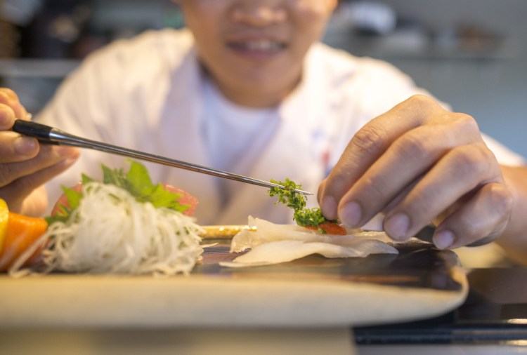 Pau Lim places scallions atop a lunch sashimi platter.
