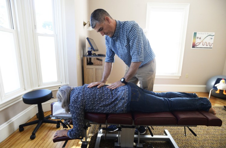 Robert Lavoie makes chiropractic adjustments to a patient, Debra Labbe of Raymond. Back injuries are on the rise for the state's  workers, according to Maine Department of Labor data.
