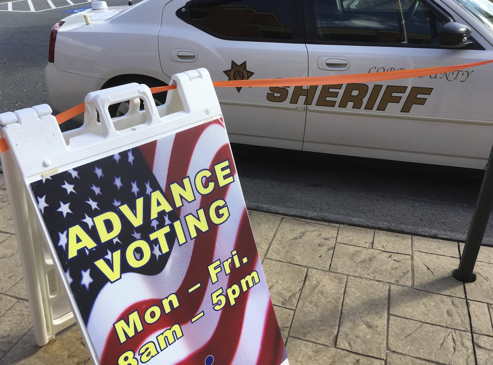 A sign displays absentee voting hours at a voting site in Marietta, Ga., as a Cobb County Sheriff's deputy sits in his vehicle Monday. Documented instances of voter fraud are extremely rare.