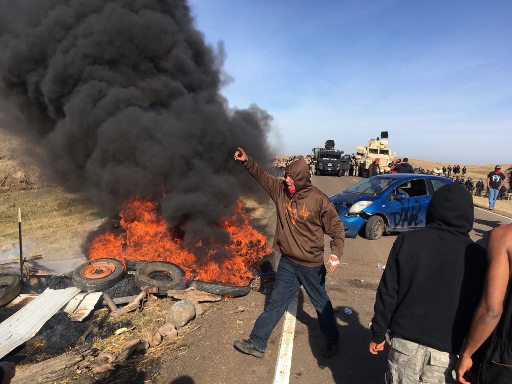 Demonstrators stand next to burning tires as armed soldiers and law enforcement officers assemble Thursday to force Dakota Access pipeline protesters off private land where they had camped to block construction. The pipeline is to carry oil from western North Dakota through South Dakota and Iowa to a pipeline in Patoka, Ill.