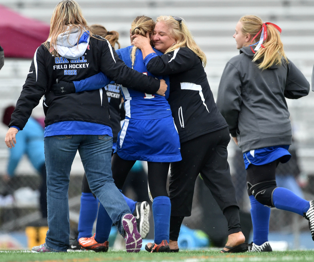 Betsy Gilbert, second from right, coach of the Oak Hill field hockey team, embraces Erika Hannifin (1) after the Raiders beat Maine Central Institute 2-0 for the Class C state championship in Bath on Saturday.
