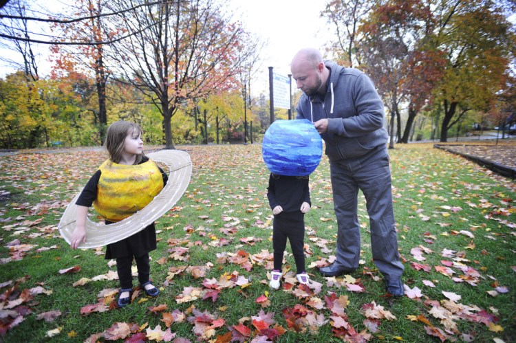 Dressed as the planet Saturn, Leah Purinton, 5, of Naples watches as her father, Stewart Purinton, helps Lydia Purinton, 2, with her Neptune costume on Friday. Data shows kids pick Halloween costumes based on hopes and dreams, but adults pick based on fear.