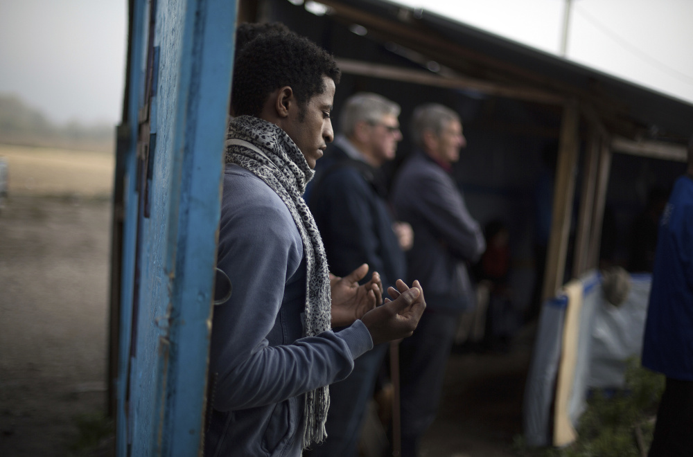 A migrant prays during the final service at a makeshift church in what remains of the squalid camp near Calais, France, on Sunday. French authorities are evacuating residents of the so-called "jungle" camp and razing its tents and shanties.