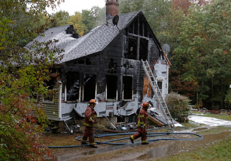 Firefighters walk past the house that burned Sunday morning in Boothbay. Two people died and four others were injured in the fire.
Joel Page/Staff Photographer