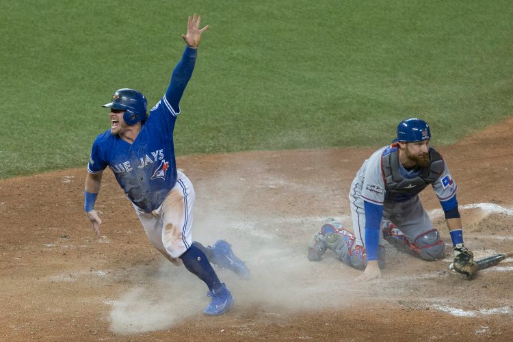 Toronto's Josh Donaldson, left, celebrates after scoring on a throwing error as Texas Rangers catcher Jonathan Lucroy kneels on the plate after the tenth inning Sunday.    Chris Young/The Canadian Press via AP