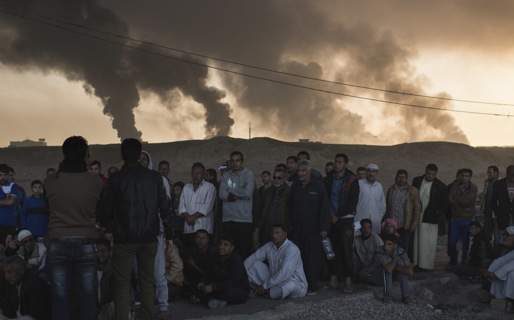 Men are held by Iraqi national security agents, to be interrogated at a checkpoint as oil fields burn in Qayara, south of Mosul, Iraq, on Saturday.