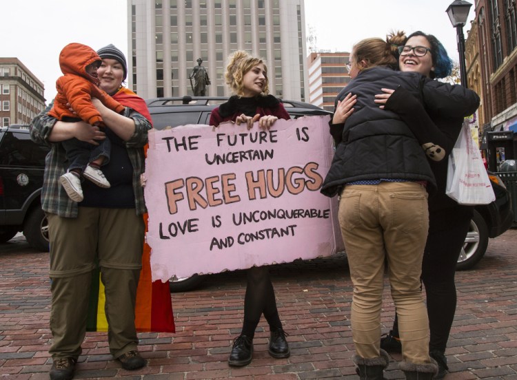 Sophie McLeod, 22, holds Gabriel Hassan, 10 months, while his mom gets a hug from Stephanie Farinhas, 21, in Portland. Donald Trump's win left McLeod, Farinhas and Jackie King, center, 21, feeling down, so they decided to offer free hugs to passersby. "I kind of needed one, so I figured everyone else could use one too," King said.