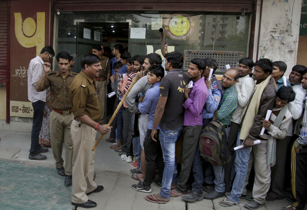 An Indian police officer warns people against breaking the queues as they wait to exchange or deposit discontinued currency notes, outside a bank near New Delhi, India, on Nov. 15.