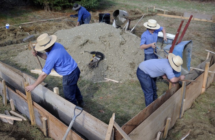 Levy Miller, left, Mose Miller and Jacob Yoder pour concrete as their uncle, John Miller, mixes it for the work shed that Mose Miller is building at the residence he purchased in Whitefield. Mose Miller and several Amish relatives are moving to Whitefield.