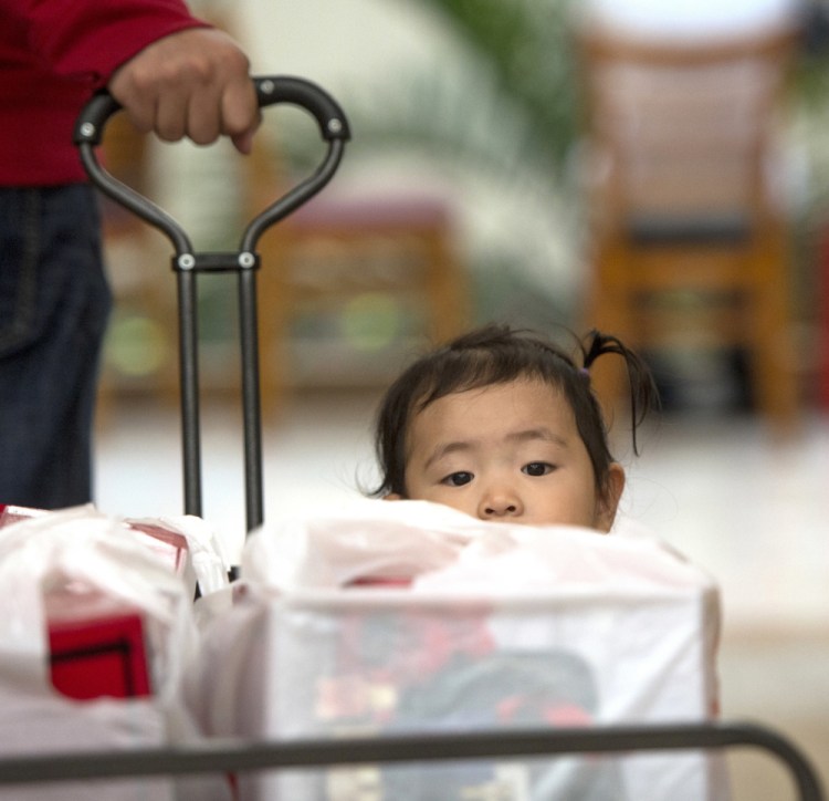 Liang Giang Ying sits in a wagon full of packages as her father pulls her through South Coast Plaza in Costa Mesa, Calif., on Black Friday.