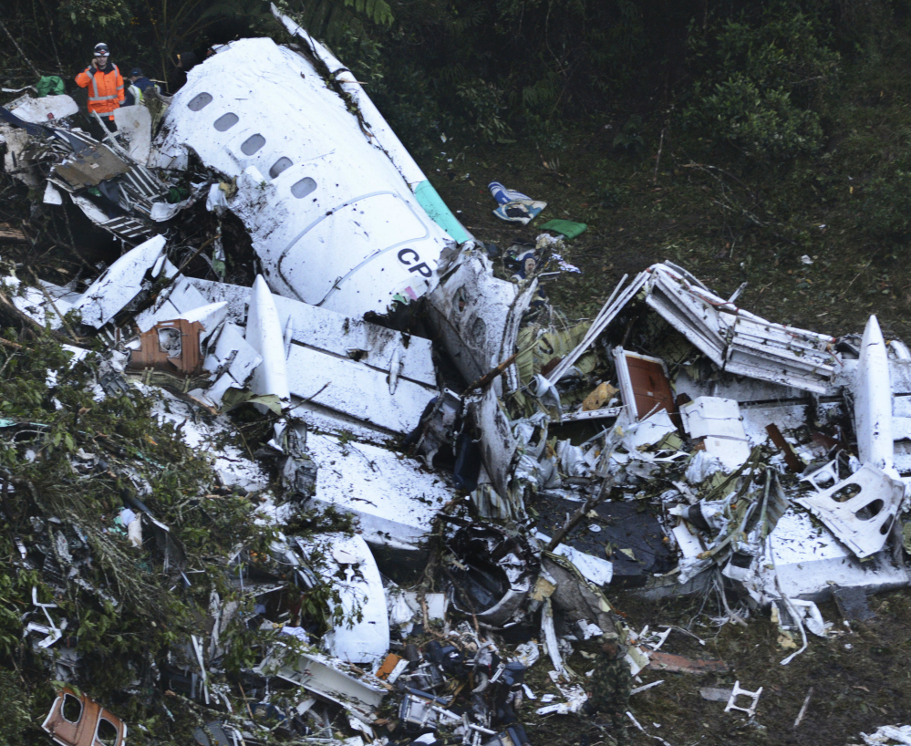Rescue workers stand at the wreckage site of the chartered airplane that crashed in a mountainous area outside Medellin, Colombia, Tuesday, killing 71 of the 77 people on board.