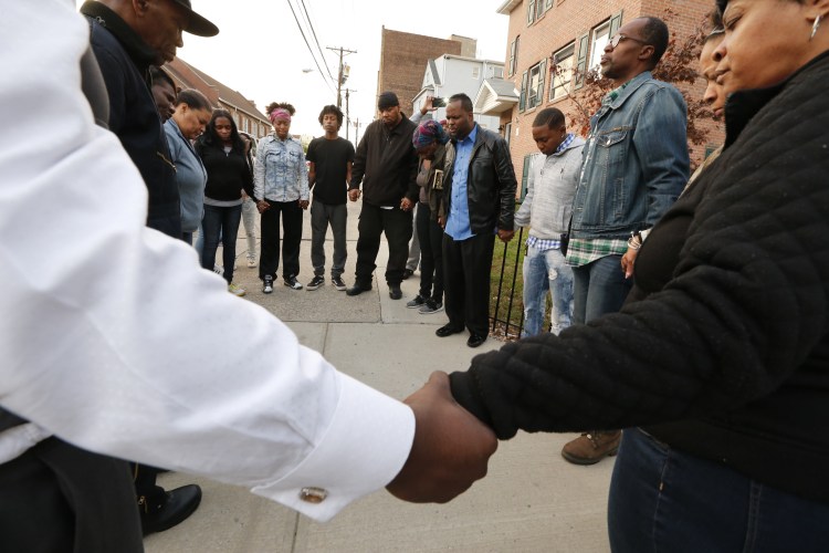 Neighbors hold hands in prayer after three people were killed and several others injured in a stabbing at a house in Newark, N.J., on Saturday. 
Robert Sciarrino/NJ Advance Media for NJ.com via AP