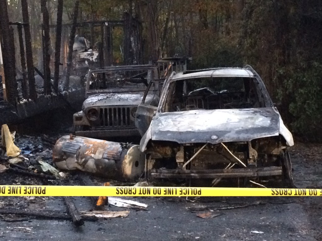 Two badly burned cars sit in the driveway next to the trailer that was destroyed in the explosion and fire. 