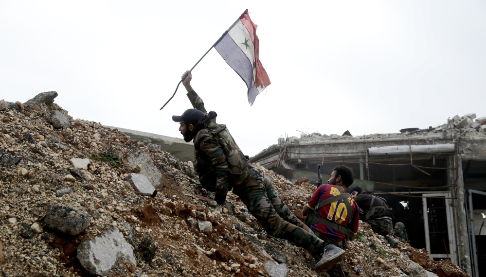 A Syrian soldier places a Syrian flag during a battle with rebel fighters at the front line, east of Aleppo, on Monday. The city appears all but recaptured by President Bashar Assad.