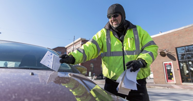 Erik Carlstrom, parking enforcement officer, sticks a ticket under a wiper blade on Commercial Street in Portland. The toughest part of the job, he says, is when conflicts arise between officers and motorists.