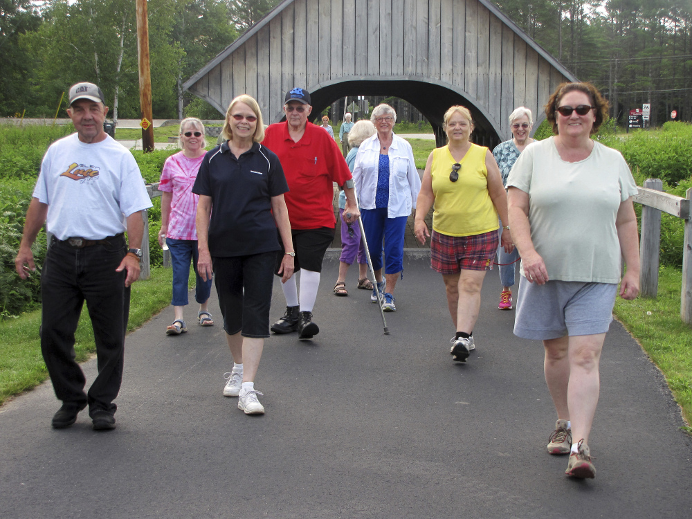 A group walks along a paved pathway in Bethel, Maine, and includes John Holliday, fourth from left wearing a red shirt. 