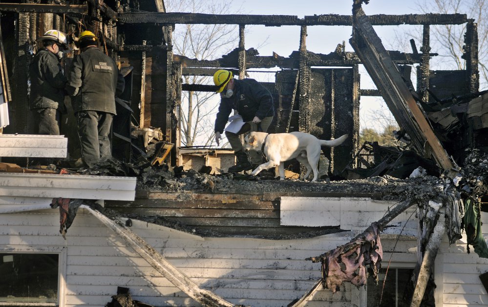 Investigators Chris Stanford, left, and Ed Archer of the state Fire Marshal's Office watch their colleague Jeremy Damren handle his accelerant-sniffing dog, Harry, while searching the burned remains of a second-floor apartment in a building in Richmond on Sunday.