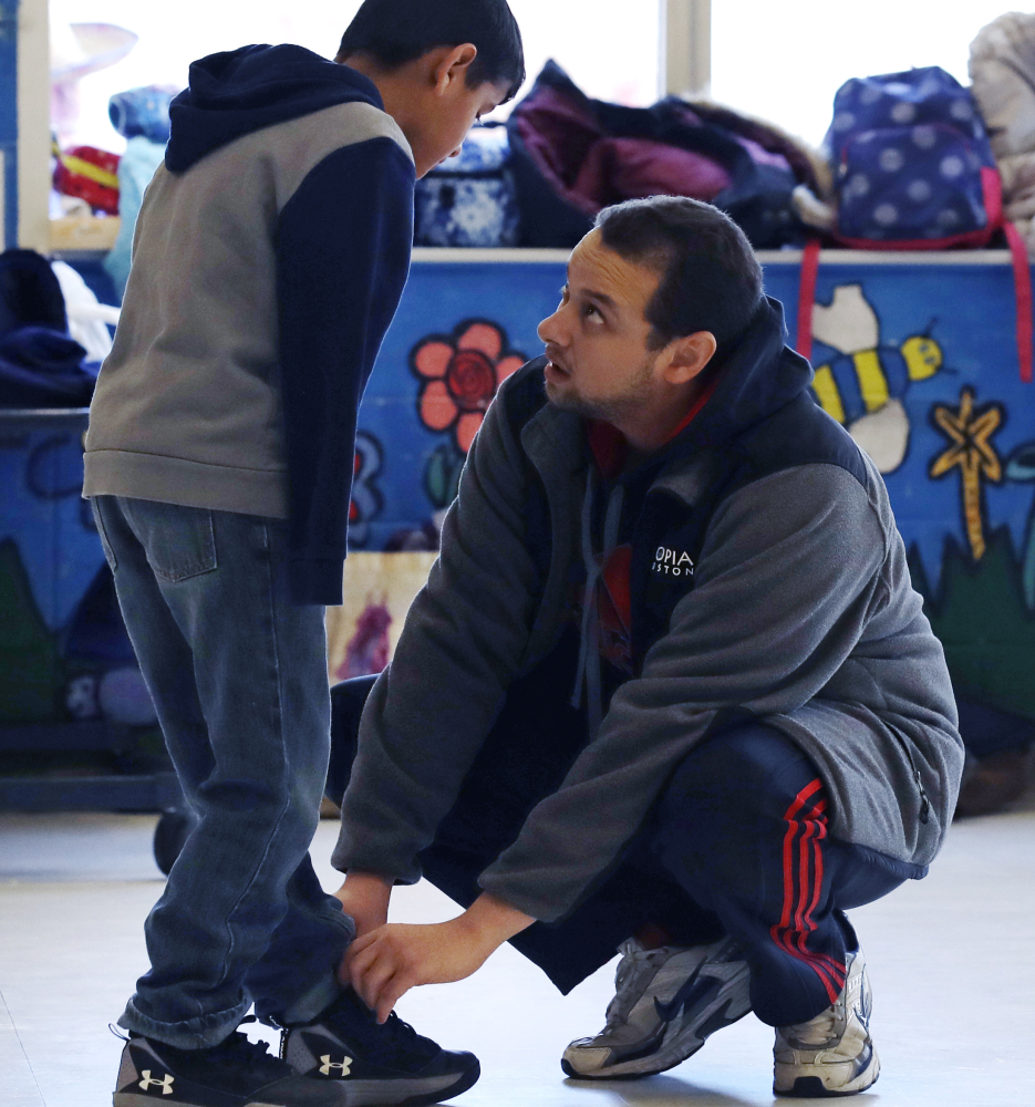 Counselor Ibrahim Hassan helps Ahmad Alkhalaf tie his shoes before the fourth-grader goes out to play soccer at day camp. Ahmad hopes to join a soccer team in the spring.
