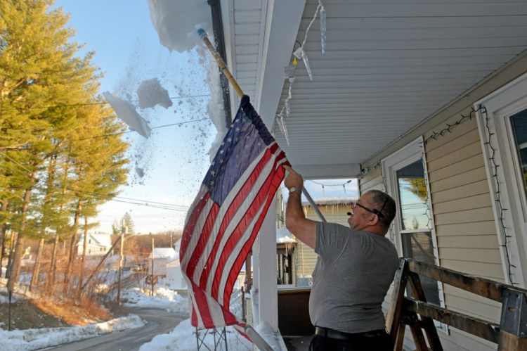 Richard Perkins clears snow and ice Thursday from the new porch roof at his residence on Redington Street in Waterville.