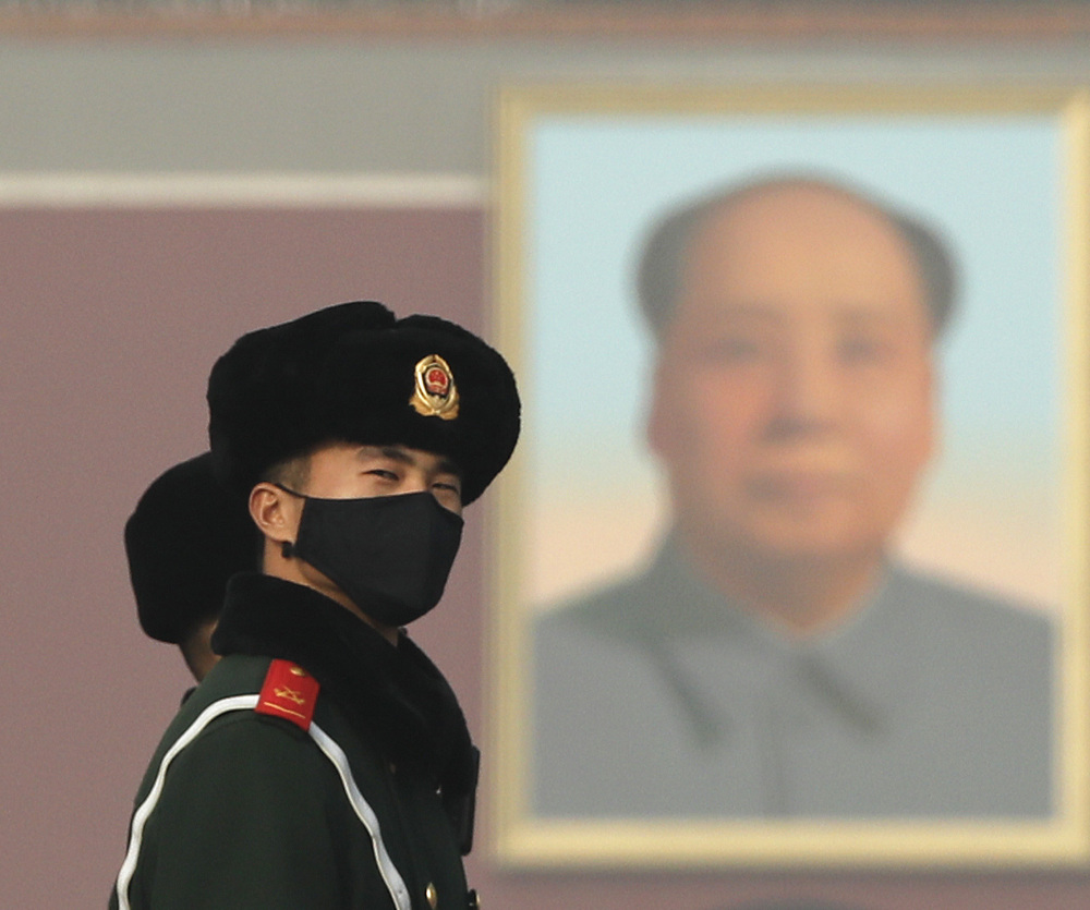 A Chinese paramilitary policeman wearing a protection mask watches visitors near a portrait of Mao Zedong at Tiananmen Square.