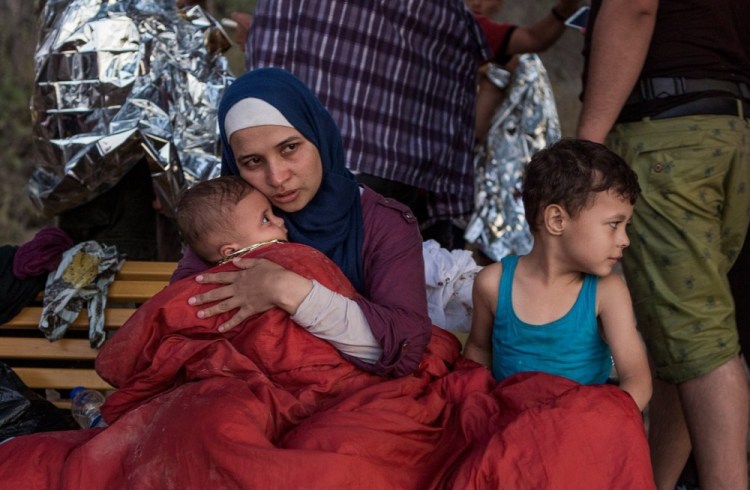 Syrian refugee Asmaa holds her 6-month old baby, Osman, while her 5-year-old, Abdul-Rahman, sits beside her in a camp in Greece. Asmaa and her husband, Omar, fled their home near Damascus last year.