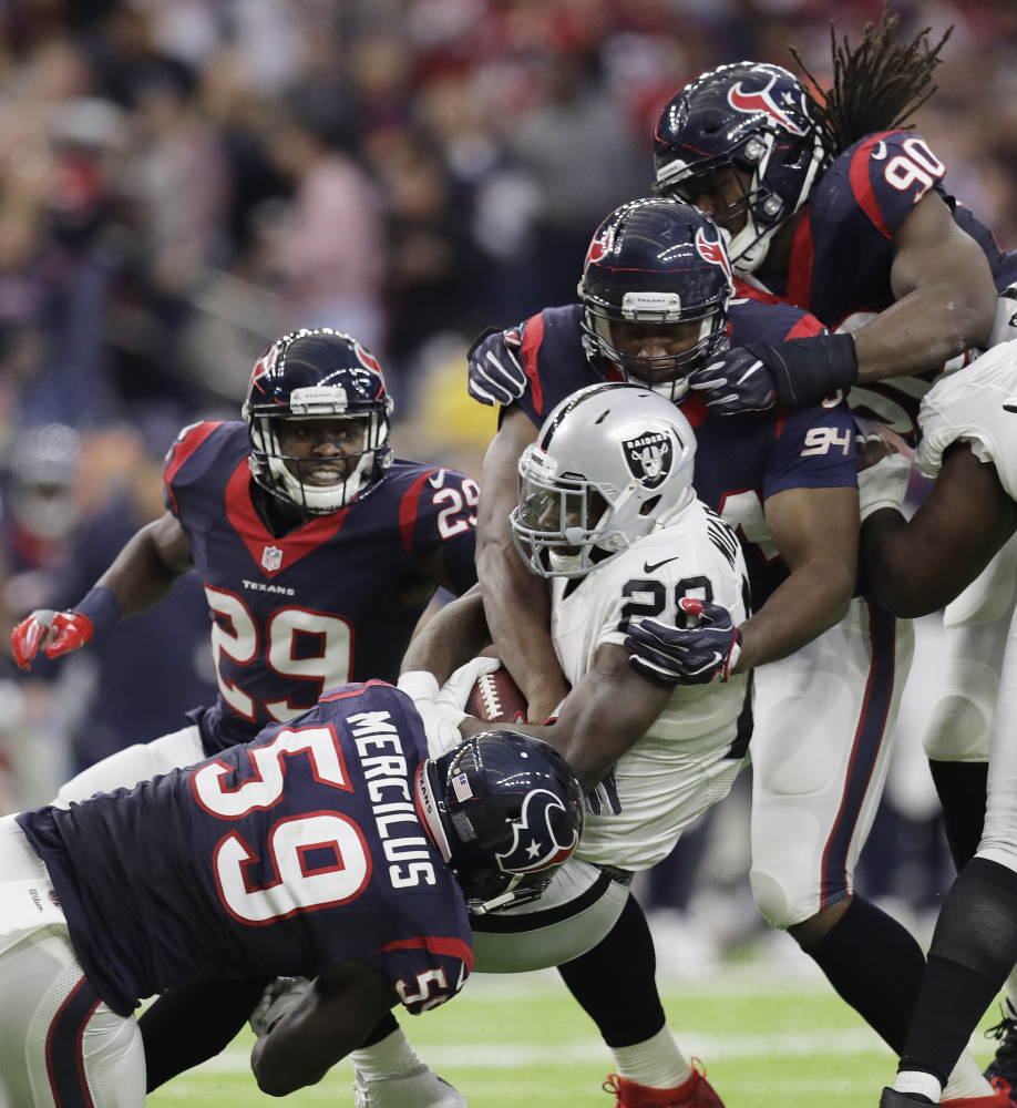 Oakland running back Latavius Murray (28) is hit by Houston's Whitney Mercilus (59) and Antonio Smith (94) during the second half Saturday game in Houston. Unless Miami beats Pittsburgh on Sunday, the Texans will play New England in the next round. (Associated Press/Eric Gay)