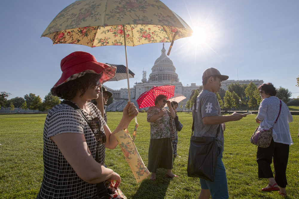 Visitors from Korea shield themselves from the early morning Augusta sun as they tour the Capitol in Washington, with temperatures lingering in upper 90s.